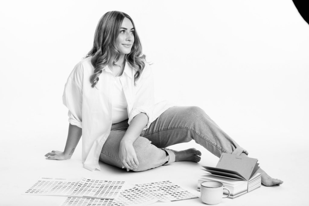 Image of Steph Honey owner of Dear Charlie Branding Studio. Sat with a white shirt, jeans and colour swatches scattered around her.
