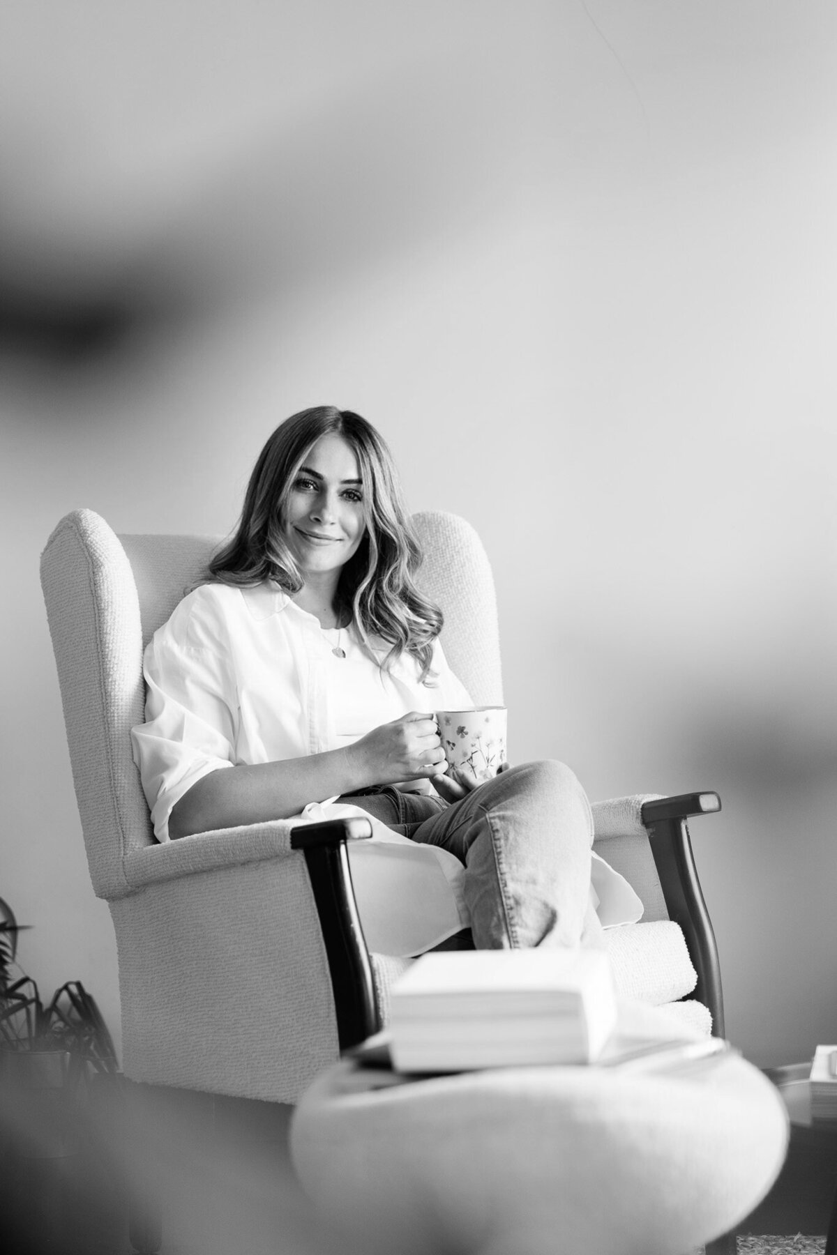 A photo of Steph honey smiling relaxedly sitting in an armchair with a cup in her hand, exuding the confident and approachable vibe essential for 'Is Your Brand Story Resonating? Here's How to Make It Unforgettable' for The Brand Essentials Podcast